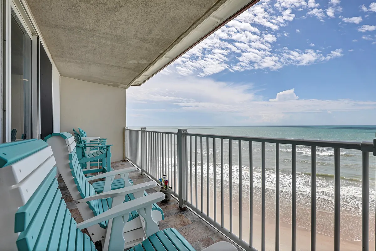 A beachfront scene featuring two turquoise chairs facing the ocean, with the sandy beach and a vast sky in the background. The setup invites relaxation and intimate moments while soaking in the ocean breeze and panoramic views.