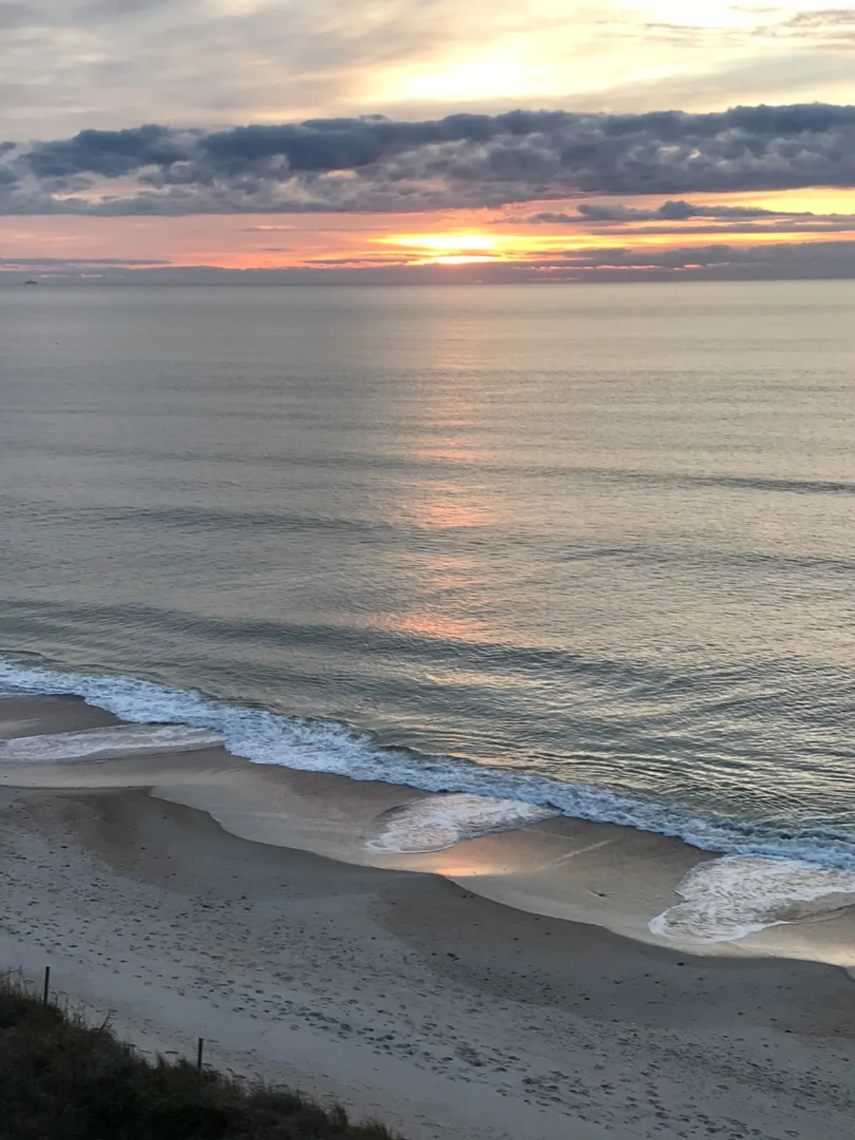A breathtaking view of the shoreline as gentle ocean waves lap the sandy beach beneath a vibrant sunset sky. The tranquil scene evokes a sense of calm and wonder.