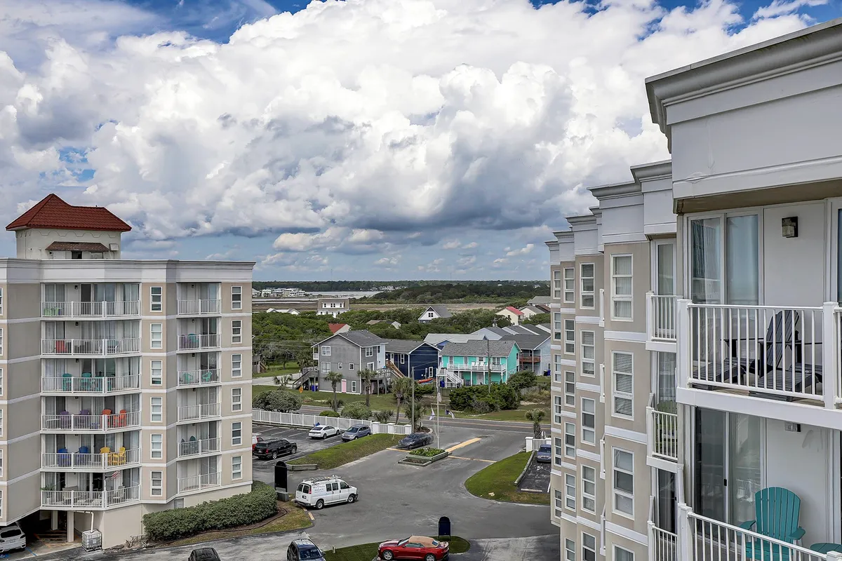 This wide-angle exterior view features colorful coastal buildings with balconies, a winding roadway, and a partially cloudy sky. The vibrant, inviting scene hints at the broader community and the opportunities for exploration in the local neighborhood near the resort.