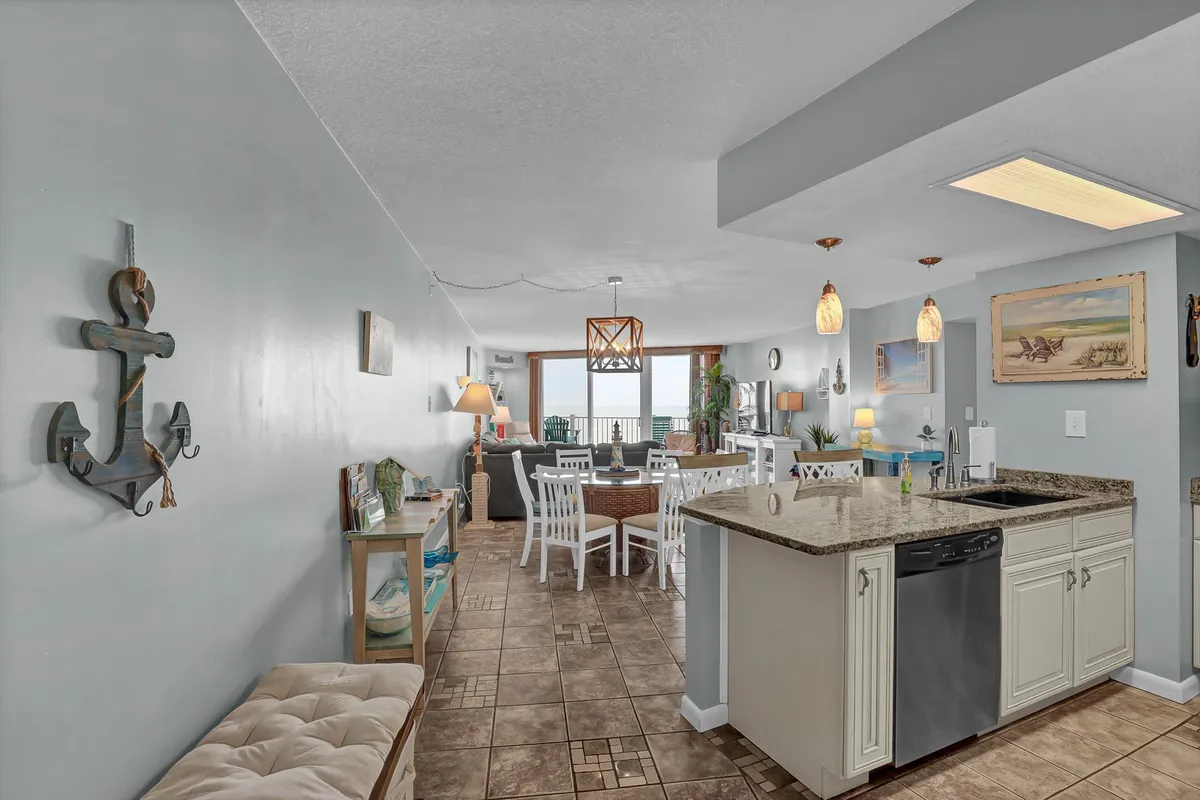A view from the kitchen area featuring a granite countertop that opens up to a dining table and a living area. The layout emphasizes the practical flow between spaces, ample storage with built-in cabinetry, and a setting well-suited for both relaxation and family gatherings.