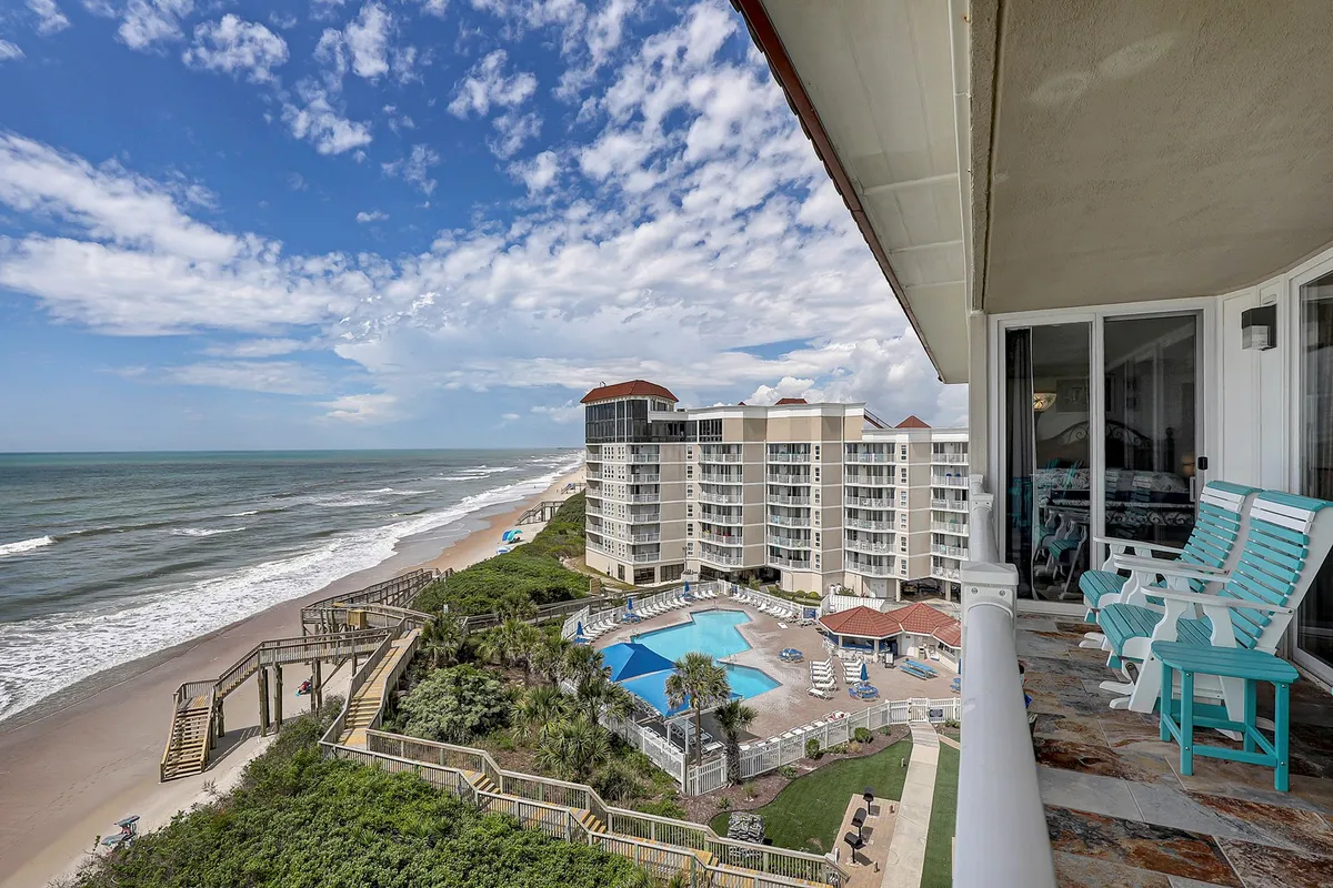 A sweeping view that captures the ocean, pool area, balcony seating, and a clear pathway leading straight to the beach. The atmosphere is serene and welcoming, highlighting convenient access from accommodations to both pools and the shoreline.