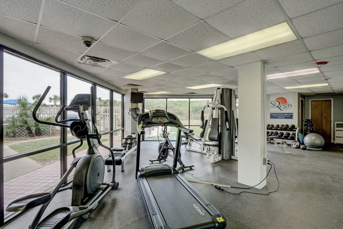 A fitness center equipped with treadmills, elliptical machines, weightlifting equipment, and large windows letting in ample natural light. The space feels energetic and health-focused, inviting guests to prioritize wellness.