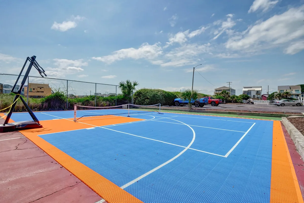 A multi-purpose sports court with a basketball hoop, tennis net, and bold court markings, set outdoors. The area invites active guests for friendly competitions and community gatherings.